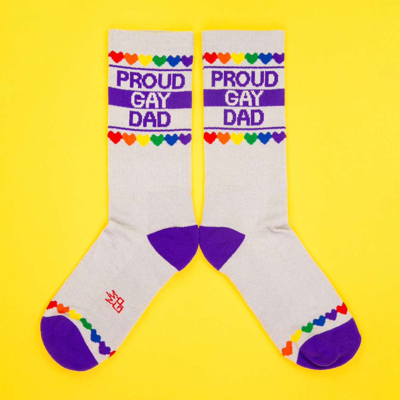 Flatlay of two 'Proud Gay Dad' socks on a yellow background, arranged parallel. [lf]