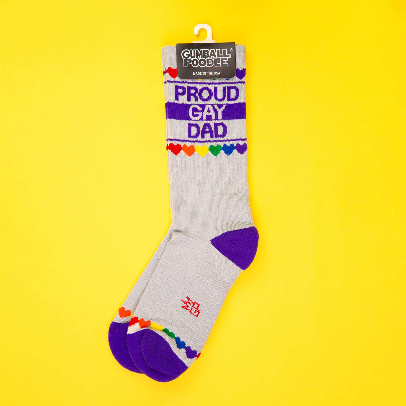 A pair of 'Proud Gay Dad' socks on a yellow background, presented with a hang tag. [lf]