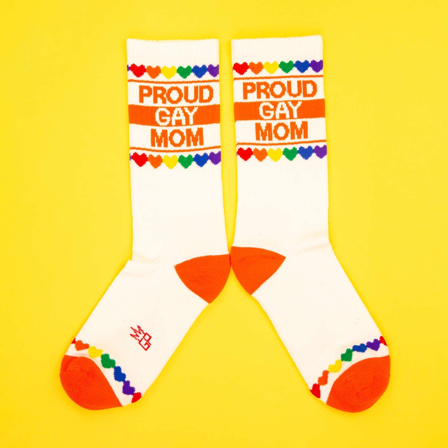 Another flatlay shot of the 'Proud Gay Mom' socks on a yellow background. Socks laid parallel. [lf]