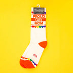Single 'Proud Gay Mom' sock on a yellow background, displayed on a hanger. [lf]