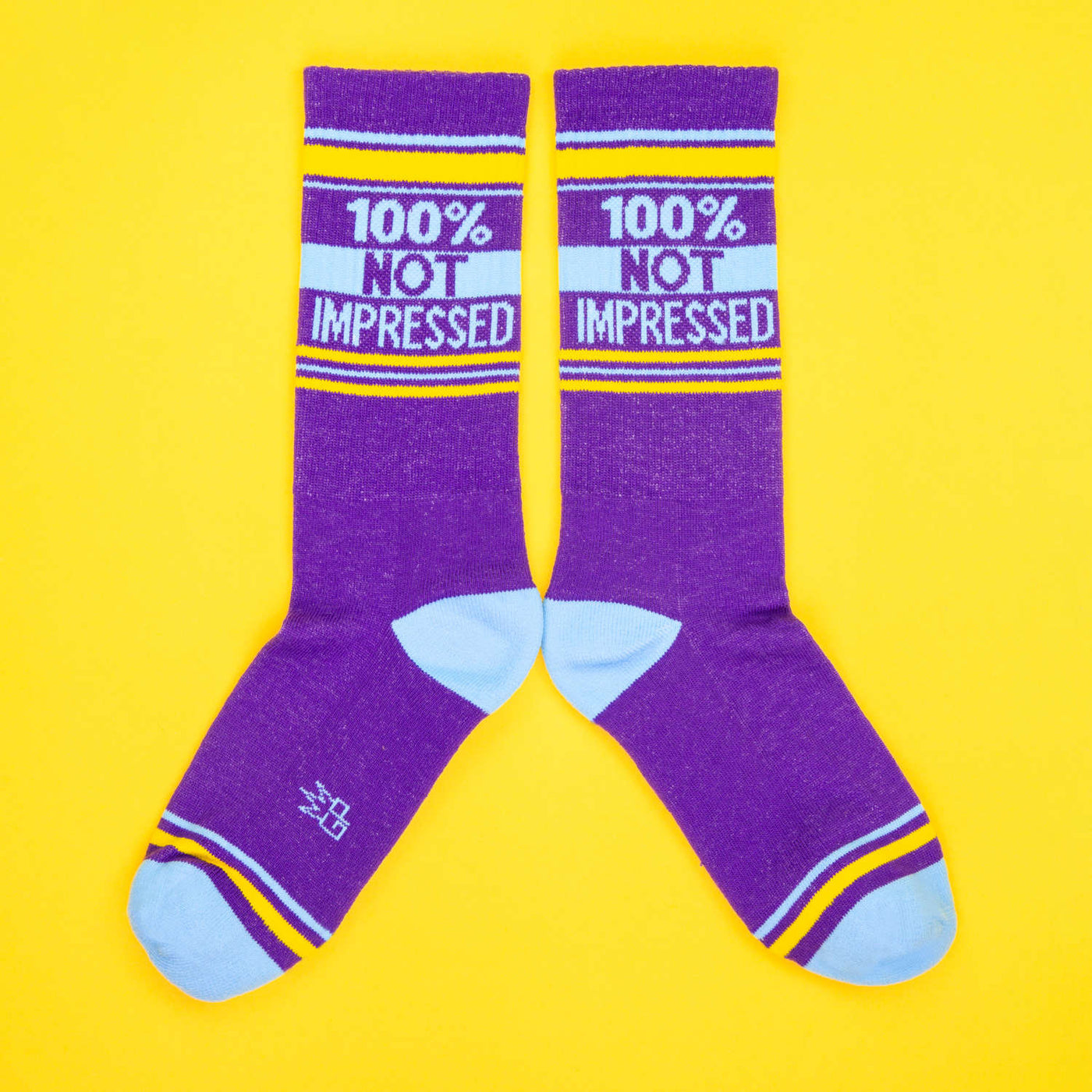 A pair of purple '100% Not Impressed' socks laid out in an X shape on a yellow background. [lf]