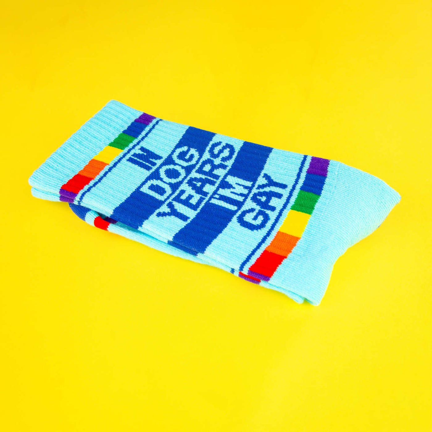 Folded 'In Dog Years I'm Gay' socks displayed on a yellow background. [lf]