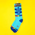 Product shot of 'In Dog Years I'm Gay' socks on a yellow background; socks are still on the packaging. [lf]