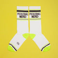 Pickleball Nerd socks on a yellow background, still on packaging. [lf]