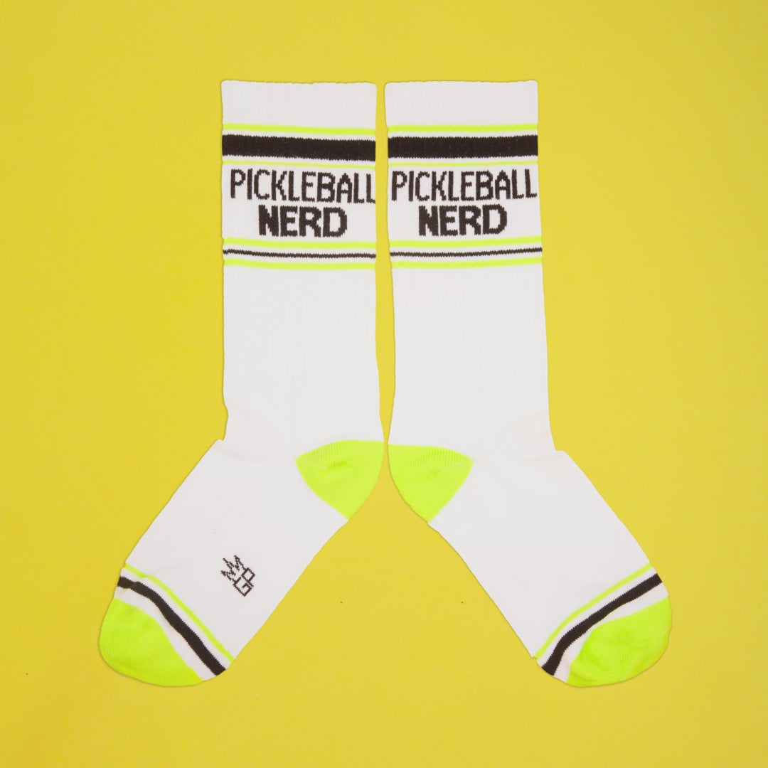 Pickleball Nerd socks on a yellow background, still on packaging. [lf]
