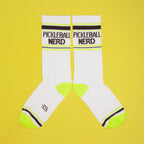 Pickleball Nerd socks on a yellow background, still on packaging. [lf]