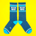 Another flatlay of teal 'Book Nerd' socks on yellow background; socks are arranged differently. [lf]