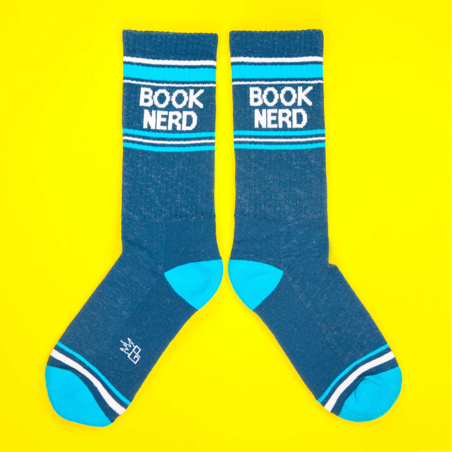 Another flatlay of teal 'Book Nerd' socks on yellow background; socks are arranged differently. [lf]