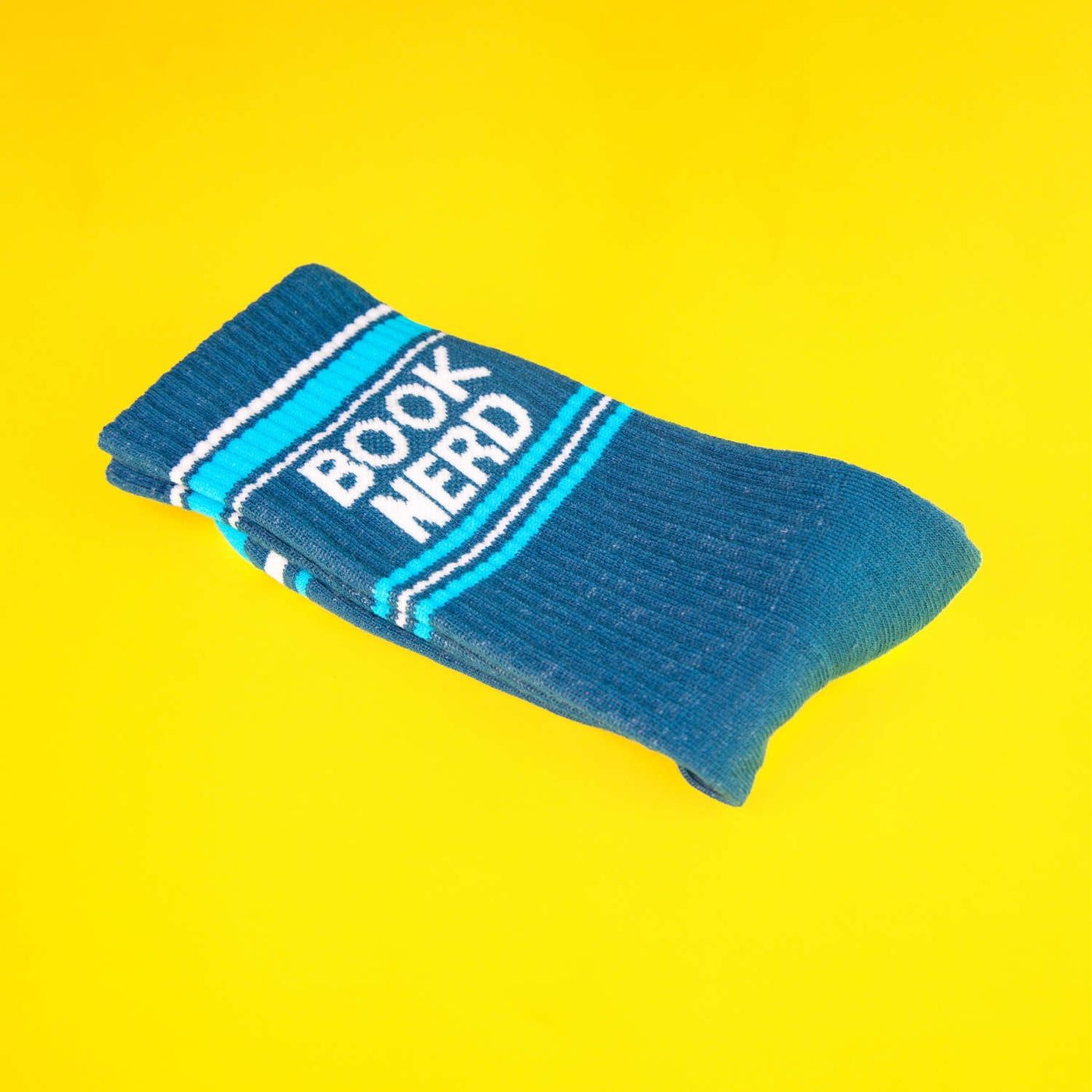 Close-up of a single teal 'Book Nerd' sock folded on a yellow background. [lf]
