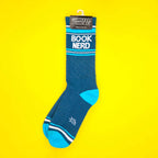 Teal 'Book Nerd' sock on yellow background, shown hanging on a tag. [lf]