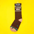 Single brown Coffee Nerd sock hanging on yellow background, showcasing the Gumball Poodle tag. [lf]