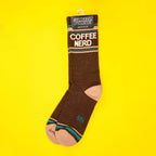 Single brown Coffee Nerd sock hanging on yellow background, showcasing the Gumball Poodle tag. [lf]