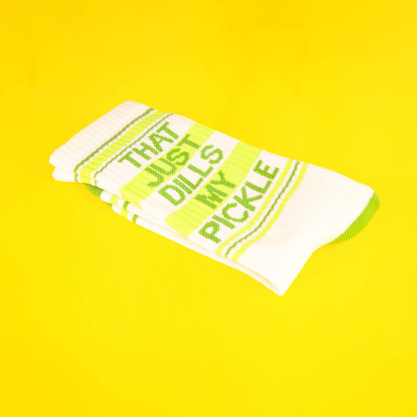 Close-up of folded 'That Just Dills My Pickle' socks on a yellow background. [lf]
