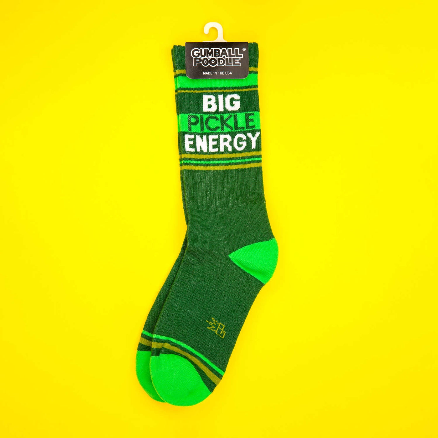 A pair of 'Big Pickle Energy' socks on a hanger with the Gumball Poodle tag visible; shown on a yellow background. [lf]