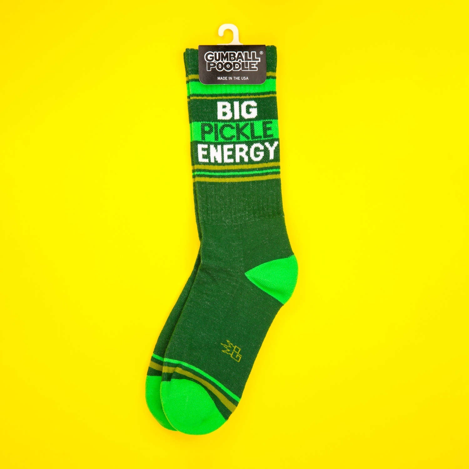 A pair of 'Big Pickle Energy' socks on a hanger with the Gumball Poodle tag visible; shown on a yellow background. [lf]