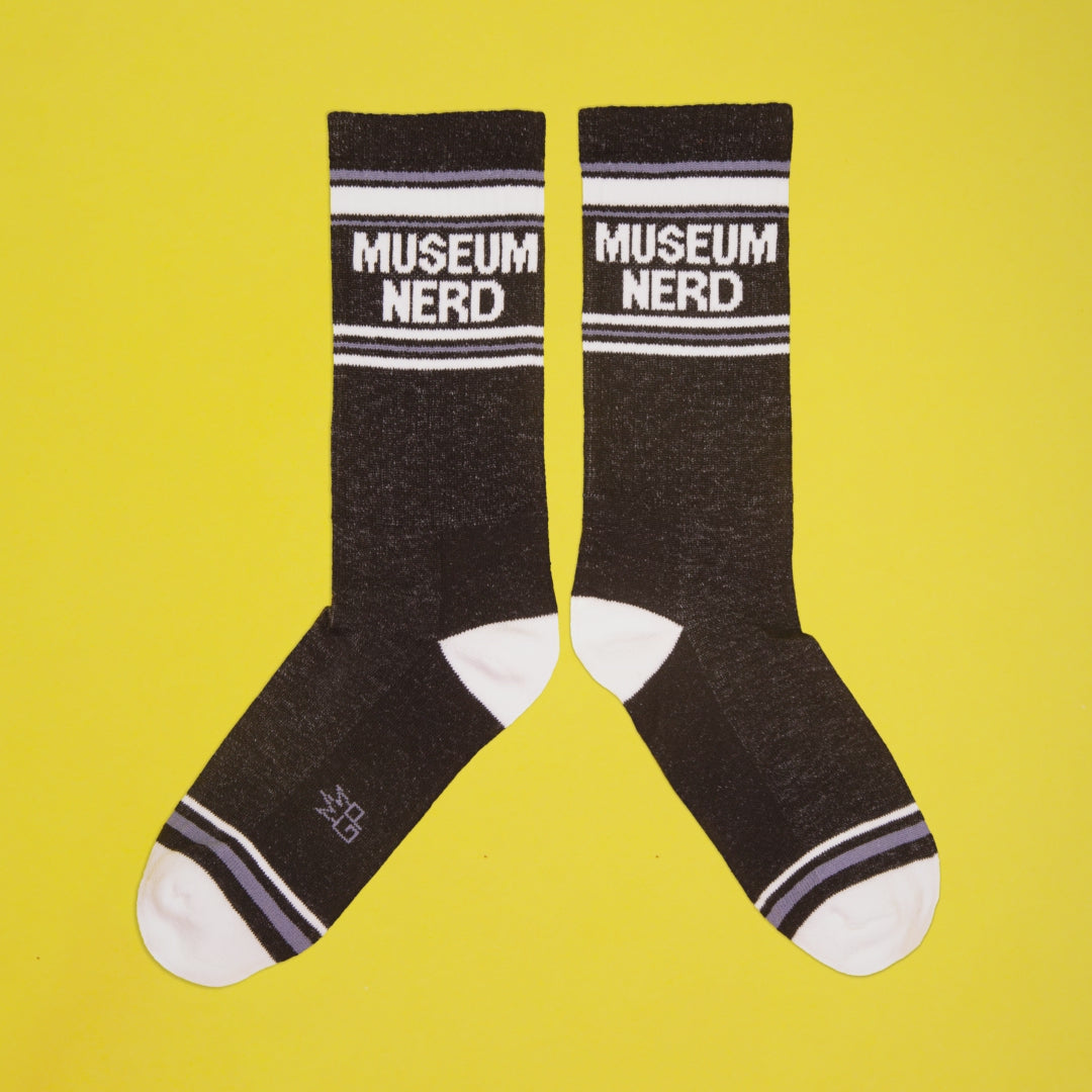 Single Museum Nerd sock on a hanger against a yellow background. [lf]