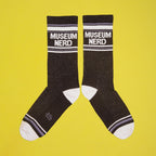 Single Museum Nerd sock on a hanger against a yellow background. [lf]