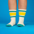 Another lifestyle shot of the Carol socks on a person's legs, standing against a bright blue background. [lf]