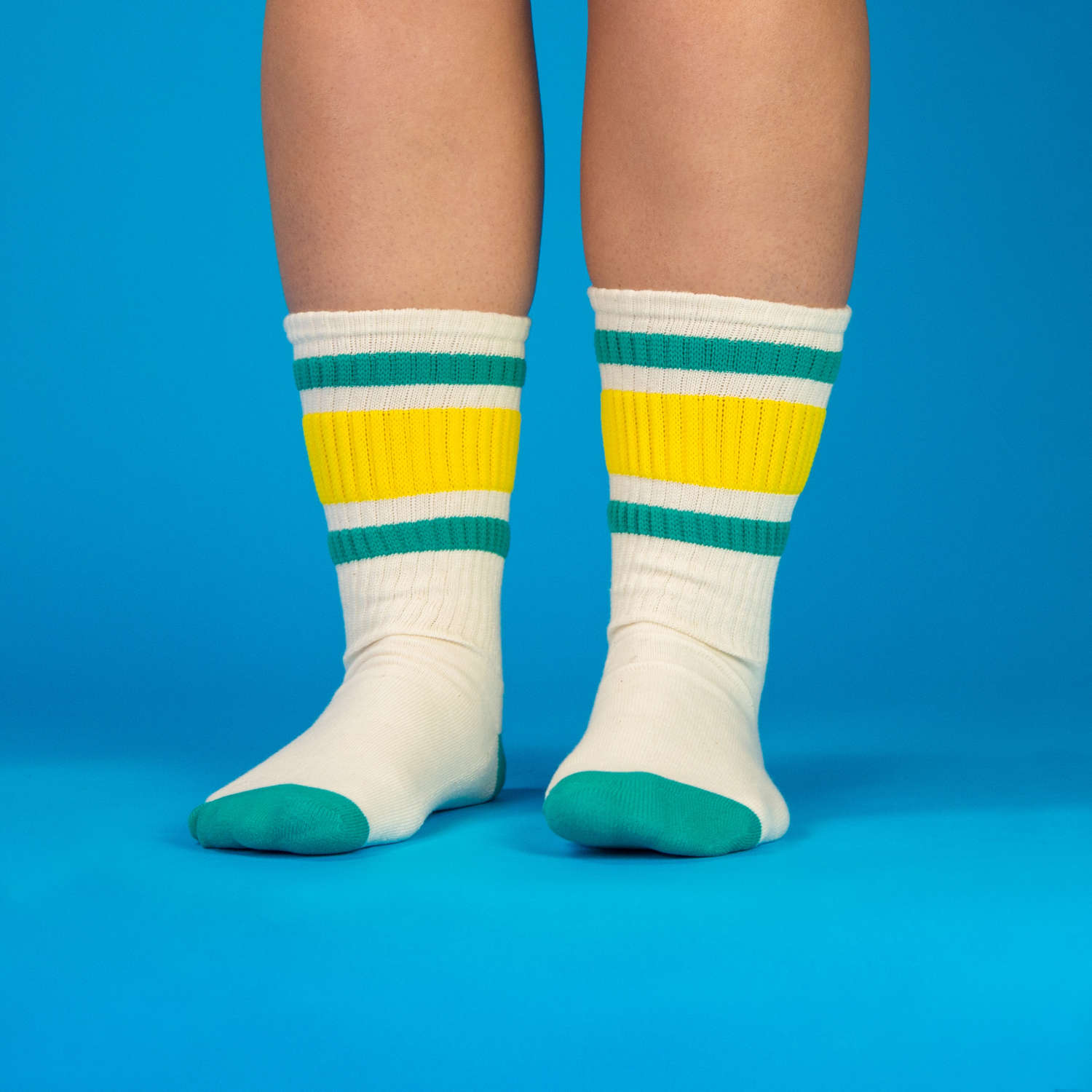Another lifestyle shot of the Carol socks on a person's legs, standing against a bright blue background. [lf]