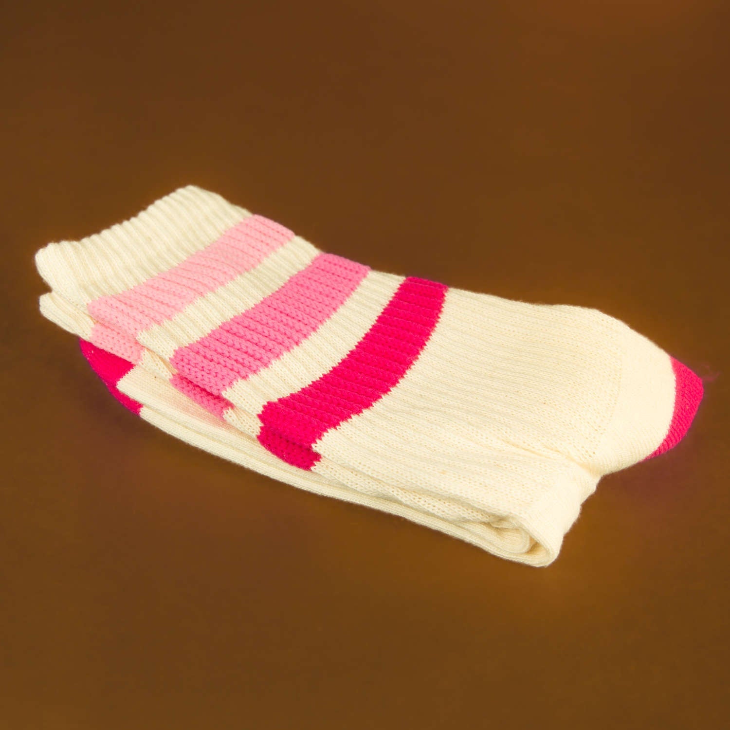 Folded cream crew socks with pink and red stripes on brown background. [lf]