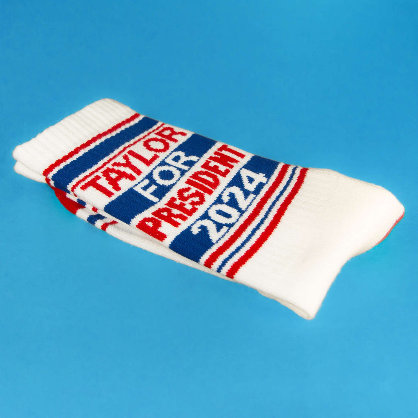 Lifestyle shot of folded 'Taylor for President 2024' socks on a blue background. [lf]