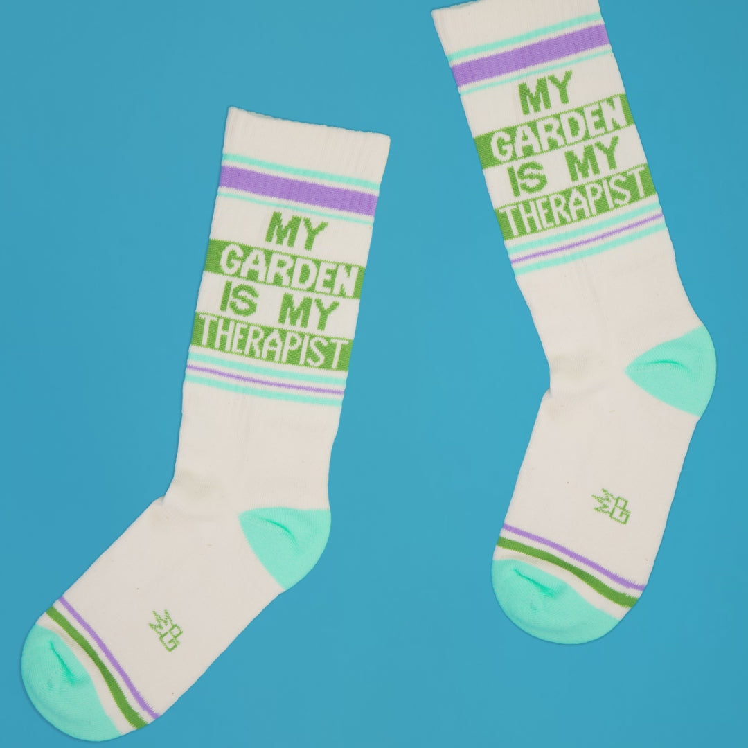Pair of 'My Garden Is My Therapist' socks arranged casually on a bright blue background. [lf]