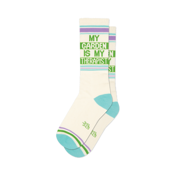 front view of a pair of white socks with green and purple stripes that say "my garden is my therapist".