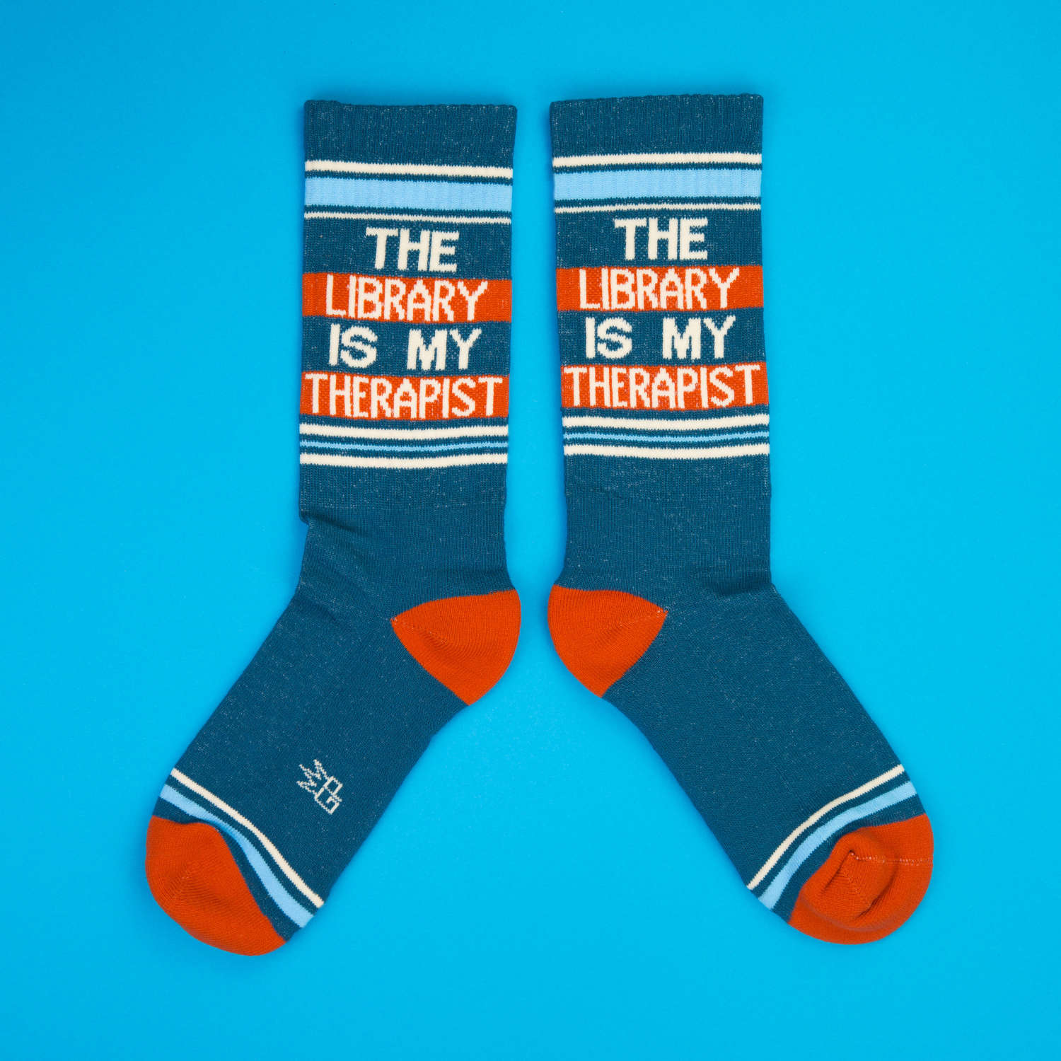 Another flat lay of teal 'The Library Is My Therapist' socks on a blue background. [lf]