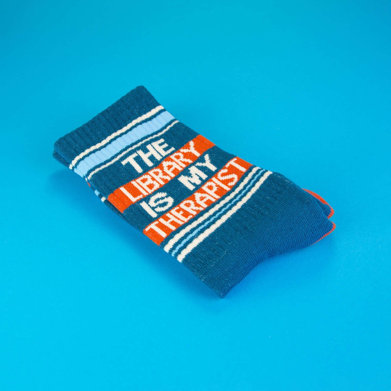Close-up of folded teal 'The Library Is My Therapist' sock on a blue background. [lf]