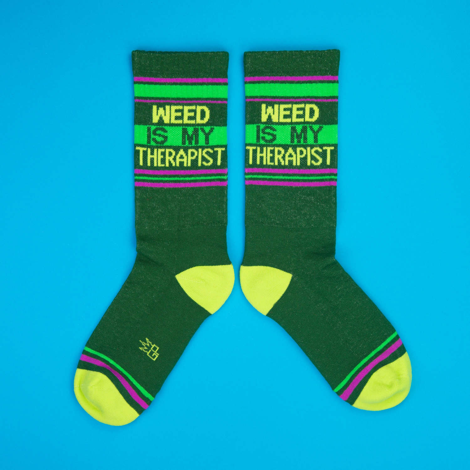 Flatlay product shot showing two 'Weed Is My Therapist' socks on a bright blue background. [lf]