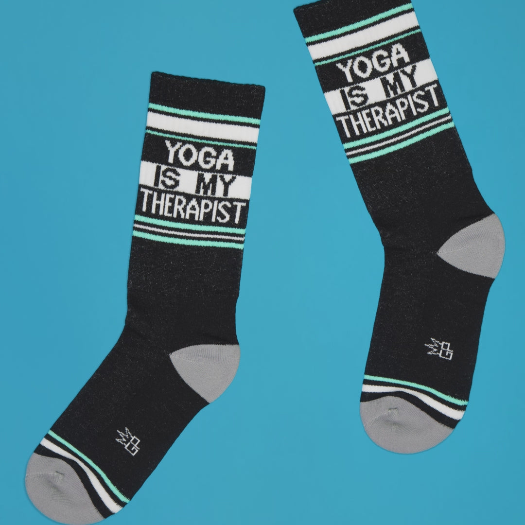 A pair of Yoga Is My Therapist socks on a blue background, angled slightly apart. [lf]