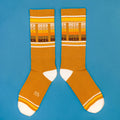 Flatlay product shot of mustard yellow 'Beer' socks on a blue background. [lf]