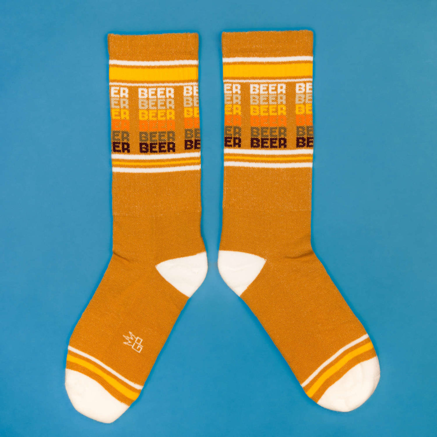 Flatlay product shot of mustard yellow 'Beer' socks on a blue background. [lf]