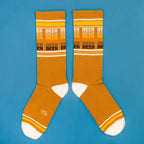 Flatlay product shot of mustard yellow 'Beer' socks on a blue background. [lf]