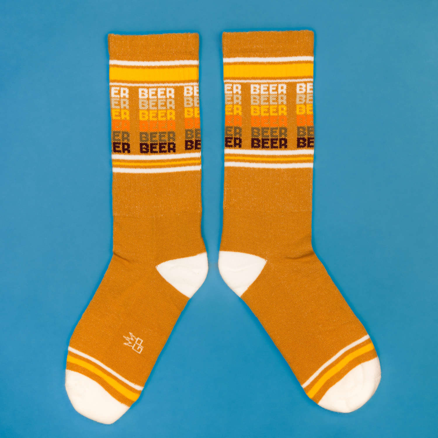 Flatlay product shot of mustard yellow 'Beer' socks on a blue background. [lf]