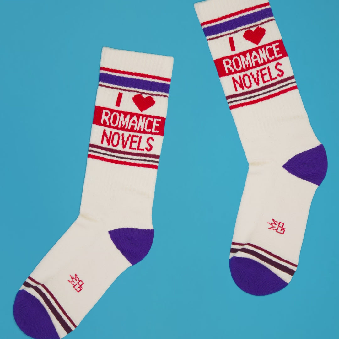 Lifestyle shot of two 'I Heart Romance Novels' socks laid on a blue background. The socks are slightly askew.