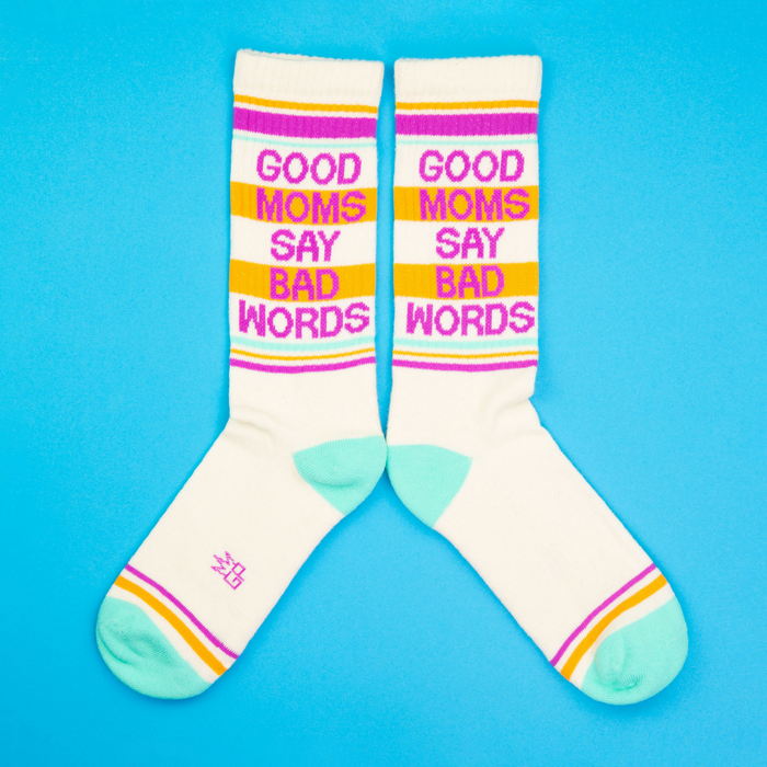 Another flatlay product shot showcasing the 'Good Moms Say Bad Words' socks, this time arranged in a more spread out position on a blue background.