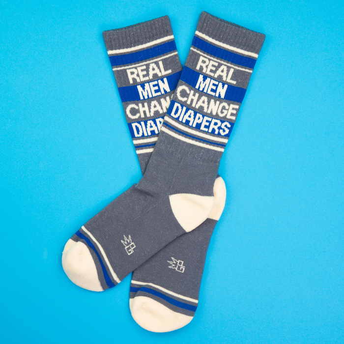 Flat lay of two 'Real Men Change Diapers' socks on a bright blue background.