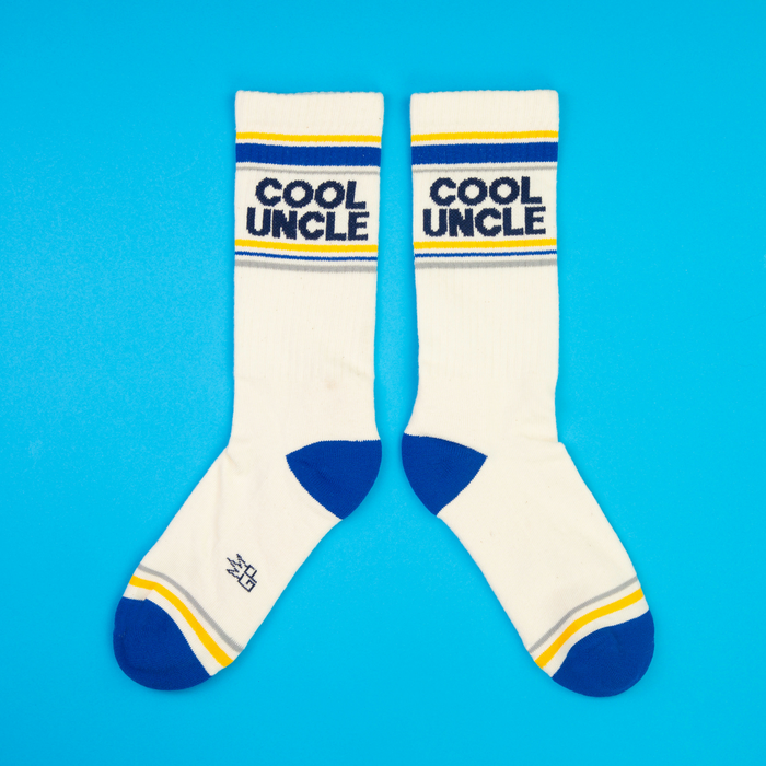 A pair of cream 'Cool Uncle' crew socks laid flat side-by-side on a bright blue background.