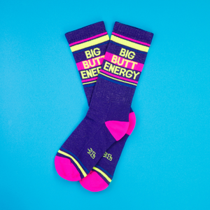 Flat lay of two 'Big Butt Energy' socks on a bright blue background.