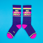 Another flat lay showing two 'Big Butt Energy' socks, arranged slightly differently on a blue background.