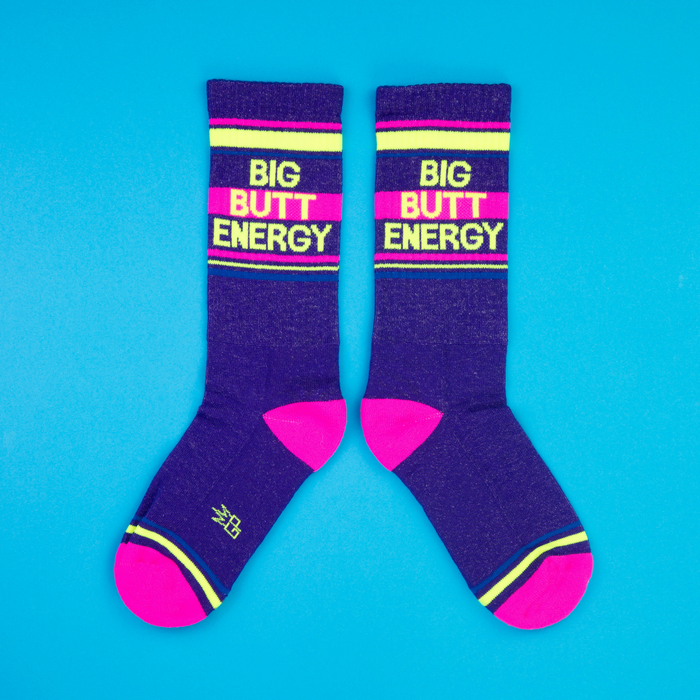 Another flat lay showing two 'Big Butt Energy' socks, arranged slightly differently on a blue background.