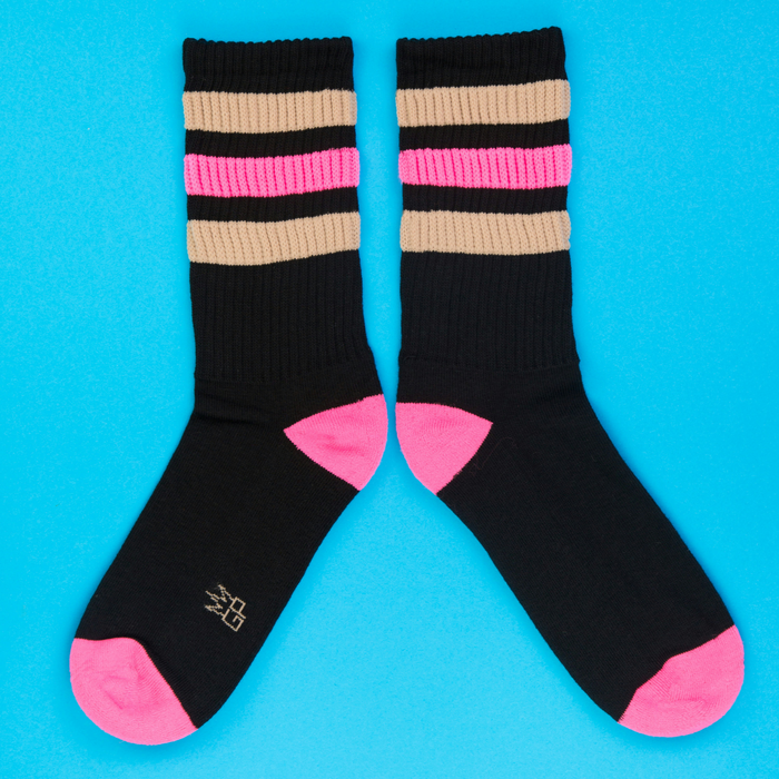 Flatlay of two Judy Retro socks on a bright blue background, showcasing the pink, beige, and black striped design.