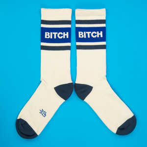 Flatlay of two 'Bitch' socks on a bright blue background.