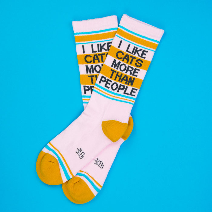 Lifestyle shot of two 'I Like Cats More Than People' socks on a blue background.