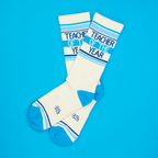 Flatlay of 'Teacher of the Year' socks on a bright blue background.