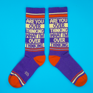 Flat lay product shot of two purple 'Are You Overthinking' crew socks on a blue background.