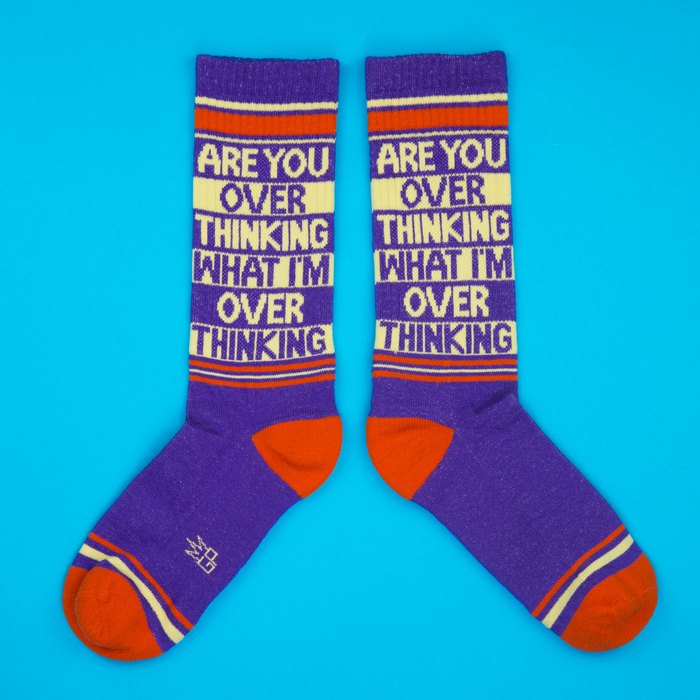 Flat lay product shot of two purple 'Are You Overthinking' crew socks on a blue background.