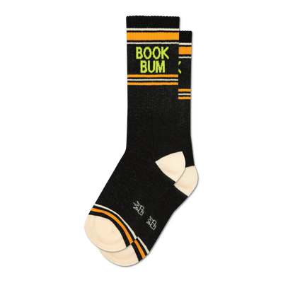 A single black crew sock standing upright, featuring neon green "BOOK BUM" text, orange and white stripes, and a cream heel and toe.