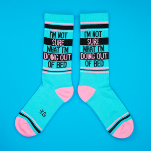 Flat lay of teal 'I'm Not Sure What I'm Doing Out Of Bed' socks against a bright blue background.